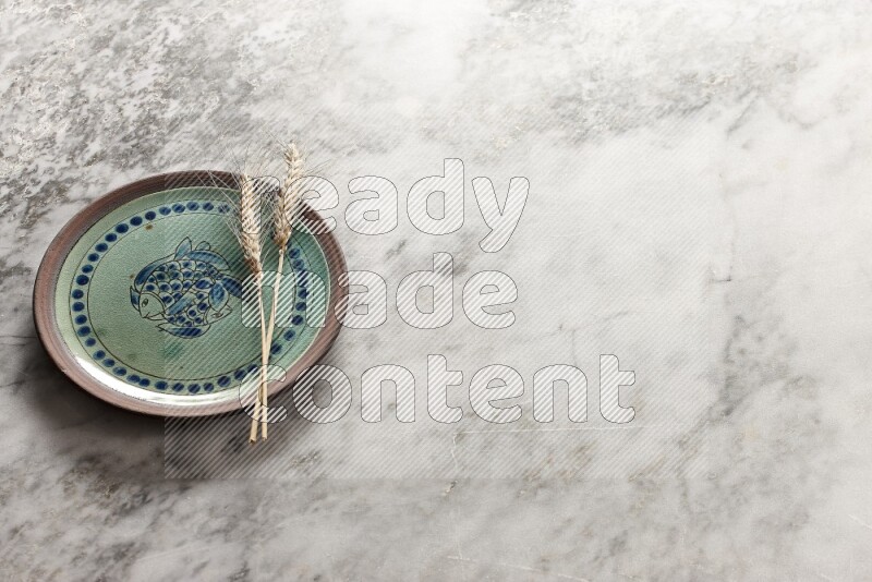 Wheat stalks on decorative pottery plate on grey marble background