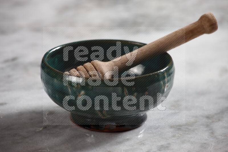 Dark green pottery bowl with wooden honey dipper in it on grey marble background