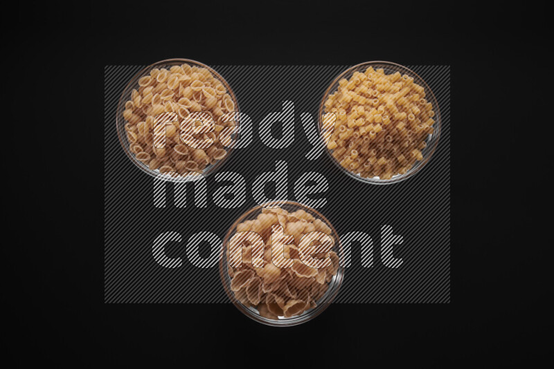 Different pasta types in glass bowls on black background