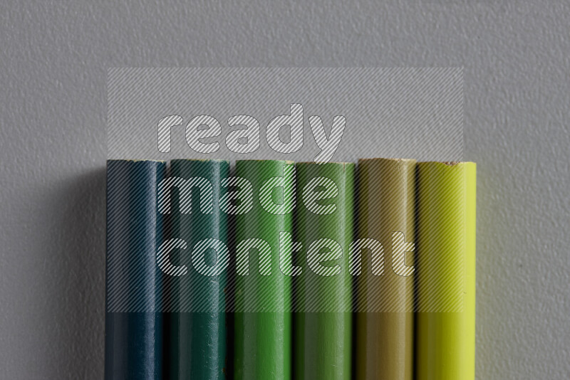 مجموعة من أقلام الرصاص الملونة مرتبة لتعرض تدرجا من الألوان الخضراء علي خلفية رمادية