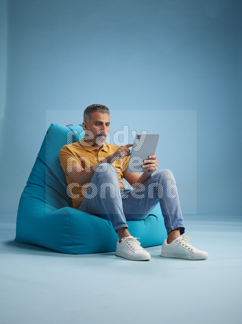 A man sitting on a blue beanbag and working on tablet