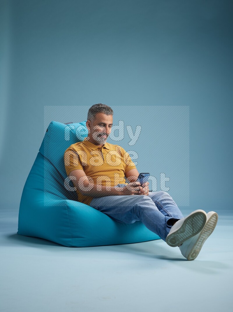 A man sitting on a blue beanbag and texting on phone