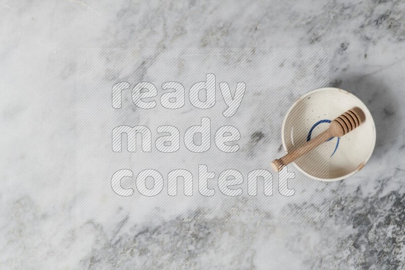 وعاء فخاري متعدد الألوان مع ملعقة عسل خشبية بداخله على خلفية من الرخام الرمادي