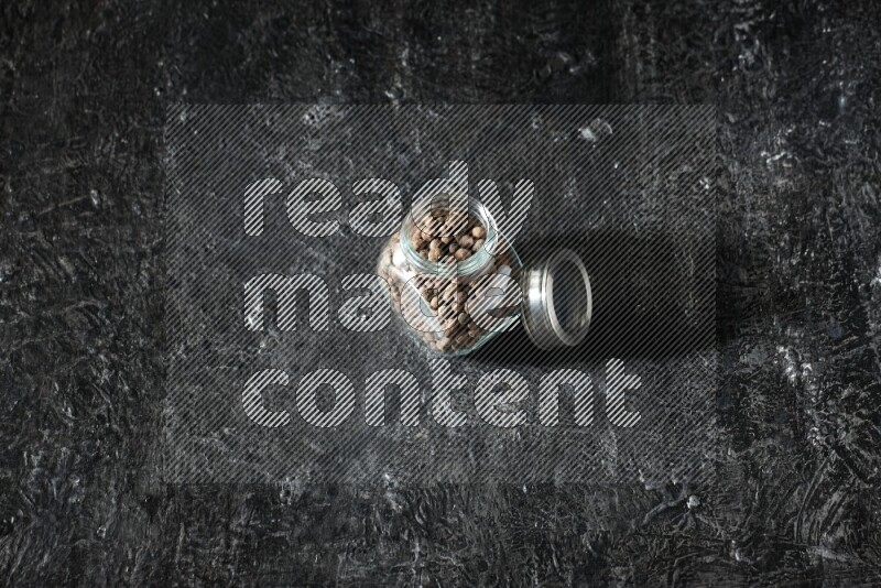 A glass spice jar full of allspice whole balls on a textured black flooring