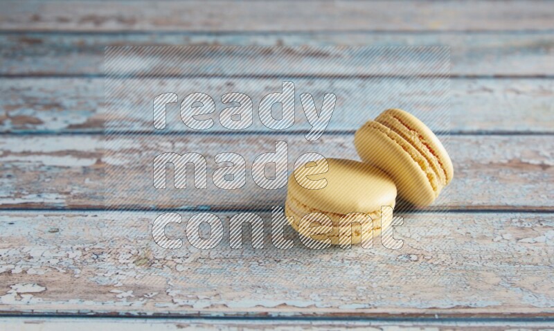 45º Shot of two Yellow Vanilla macarons on a light blue wooden background