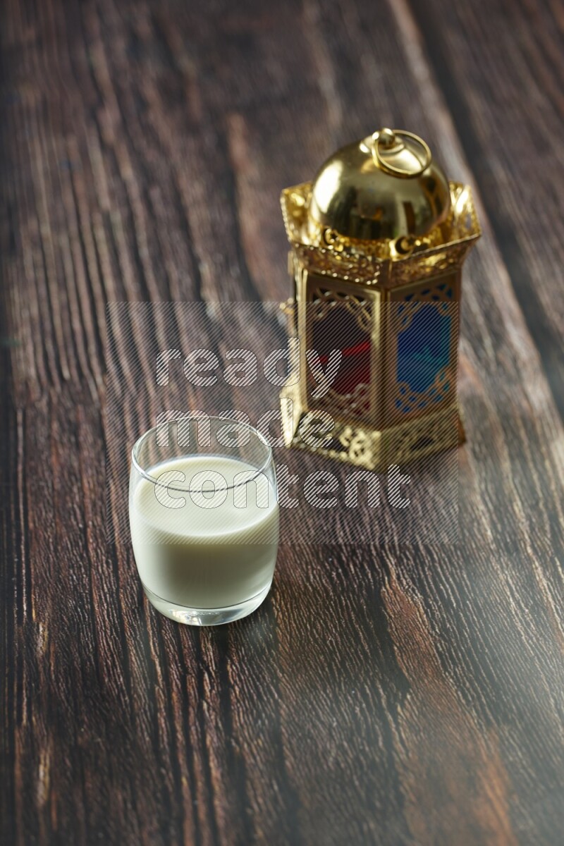 A golden lantern with different drinks, dates, nuts, prayer beads and quran on brown wooden background