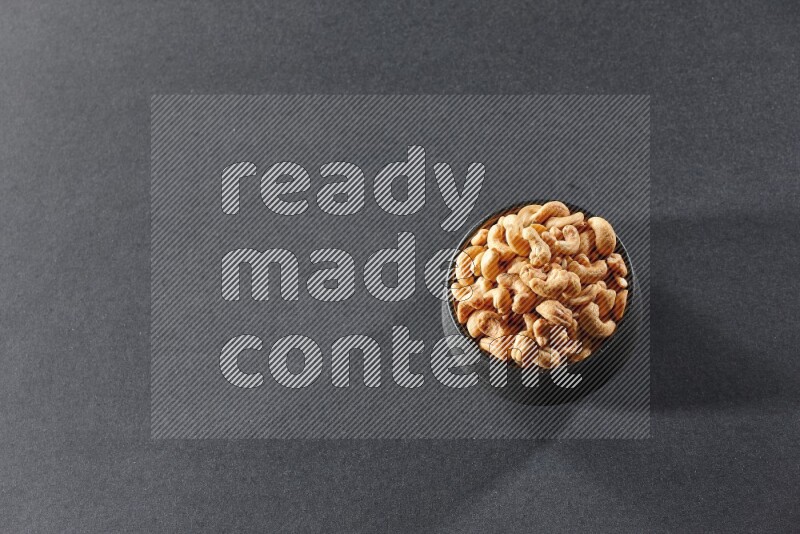 A black pottery bowl full of cashews on a black background in different angles