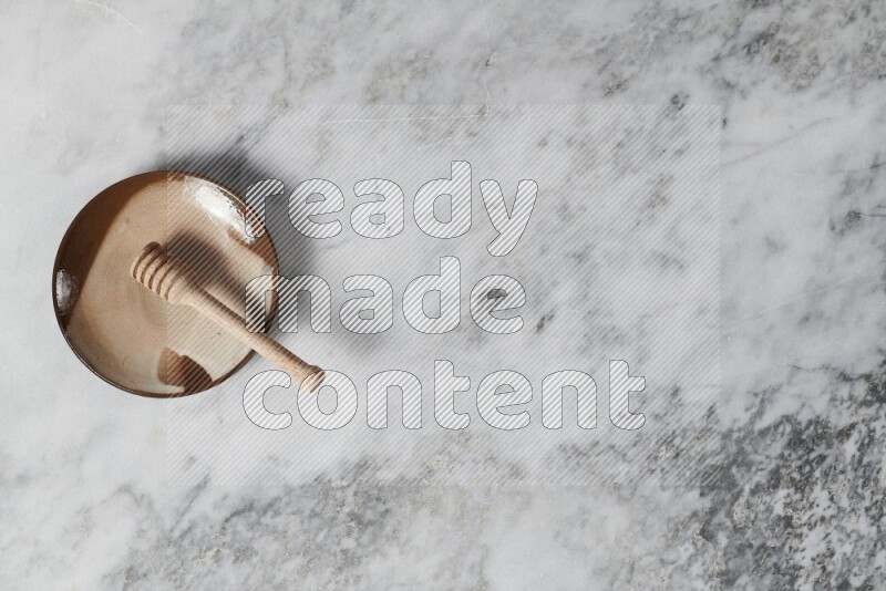 طبق فخاري متعدد الألوان مع ملعقة عسل خشبية بداخله على خلفية من الرخام الرمادي