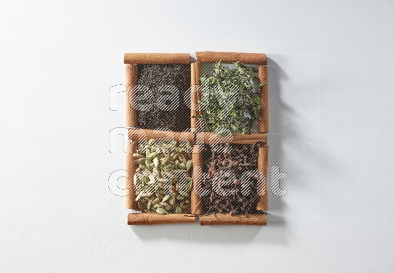 4 مربعات من أعواد القرفة ممتلئة بالشاي والهيل والنعناع والقرنفل على أرضية بيضاء