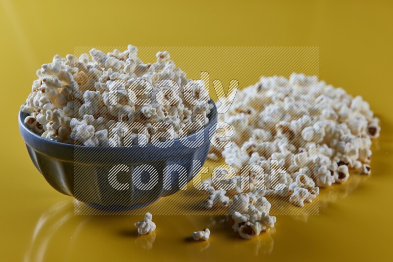 A blue pottery bowl full of popcorn with popcorn beside it on a yellow background in different angles