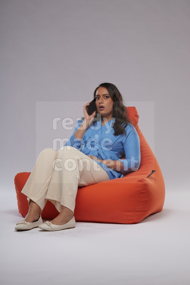 A woman sitting on an orange beanbag and talking on the phone