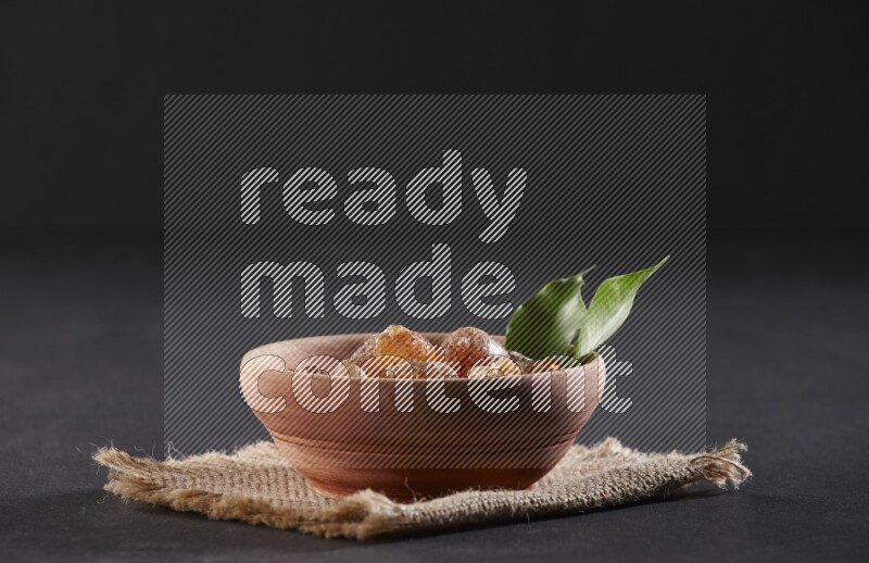 A wooden bowl full of gum arabic on a piece of burlap on black flooring