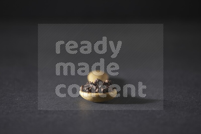 A wooden spoon full of cloves on a black flooring