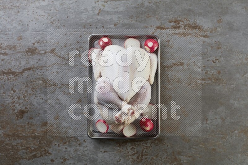whole Raw chicken on a small oven trey direct on a rustic grey background