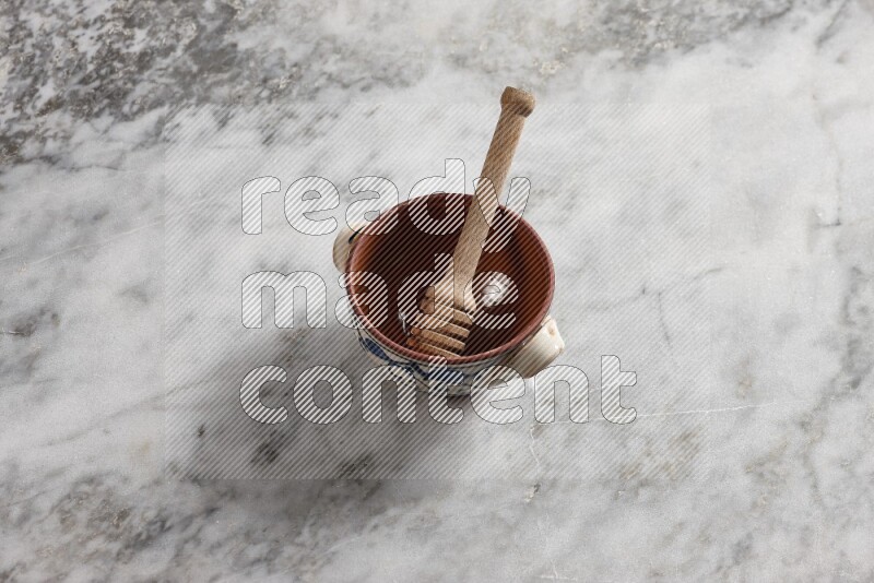 Decorative pottery pot with wooden honey dipper in it on grey marble background
