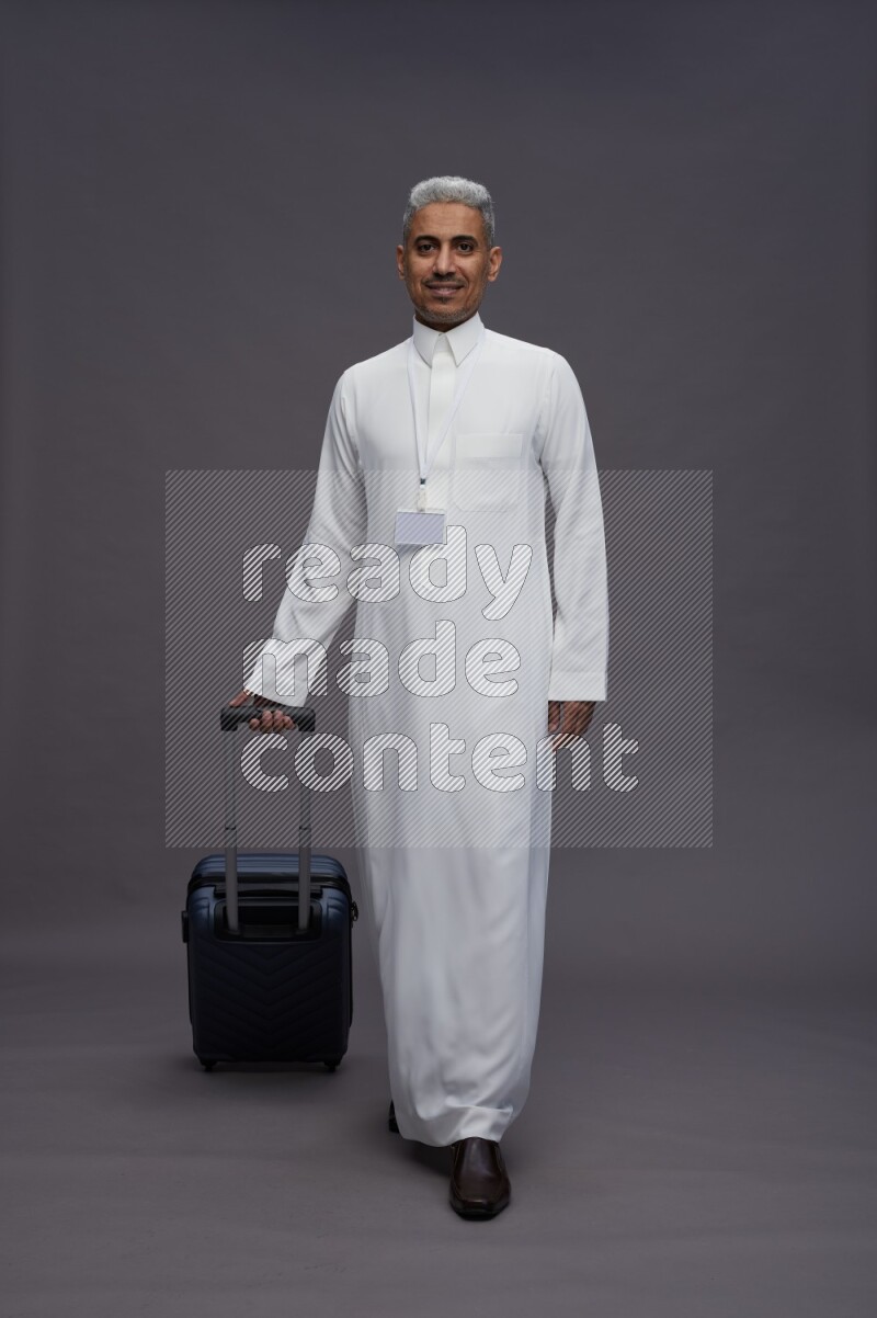 Saudi man wearing thob with neck strap employee badge standing holding bag on gray background