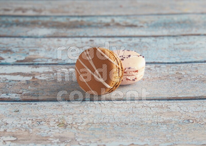 45º Shot of of two assorted Brown Irish Cream, and pink orange blossom  macarons on light blue background