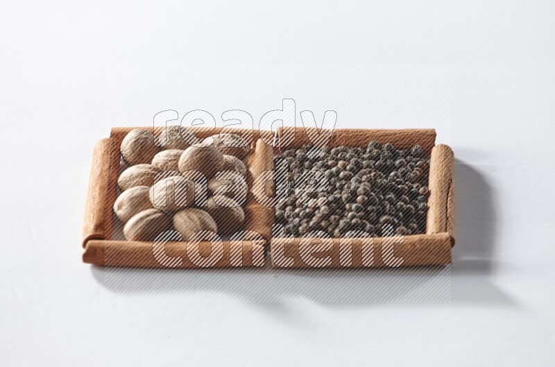 مربعان من أعواد القرفة ممتلئان بحبوب الفلفل الأسود وجوزة الطيب علي خلفية بيضاء