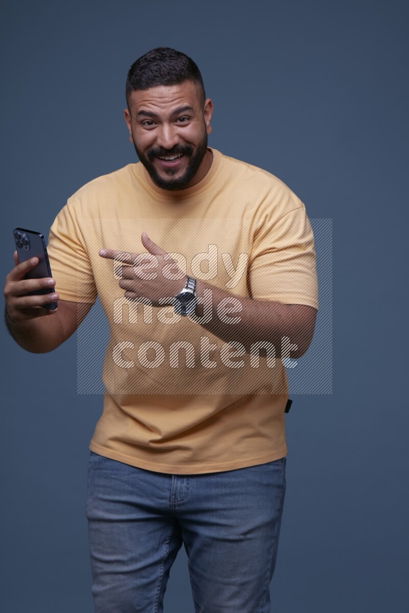A man Pointing at a Smartphone on Blue Background wearing Orange T-shirt