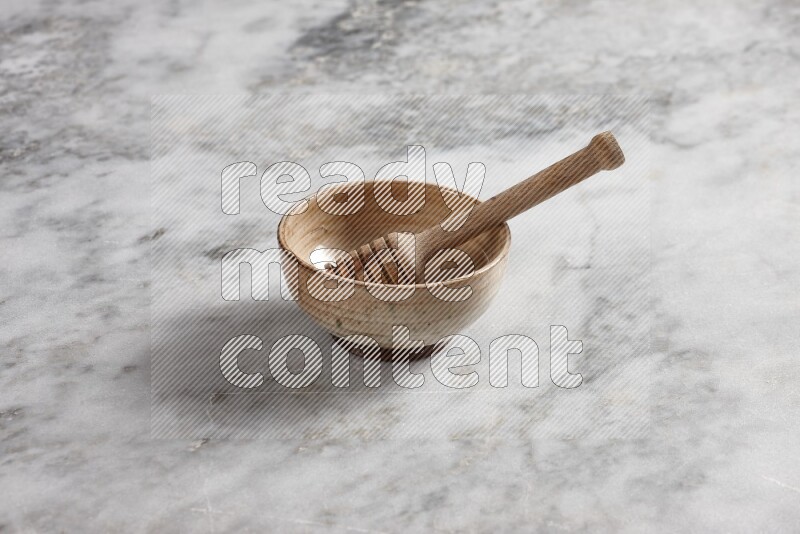 Beige pottery bowl with wooden honey dipper in it on grey marble background