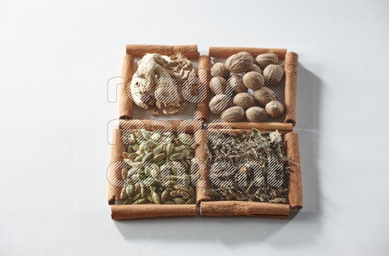 4 مربعات من أعواد القرفة ممتلئة بجوزة الطيب والزنجبيل المجفف والهيل والريحان المجفف على أرضية بيضاء