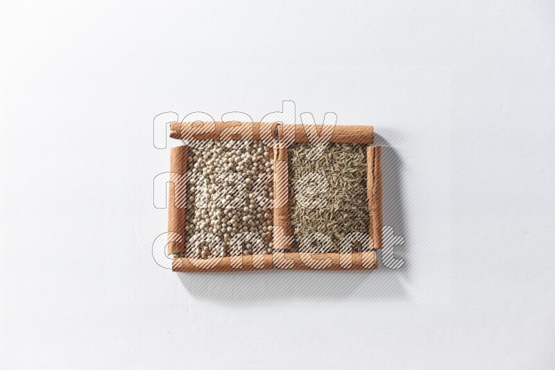 مربعان من أعواد القرفة ممتلئان بحبوب الفلفل الأبيض وحبوب الكمون علي خلفية بيضاء