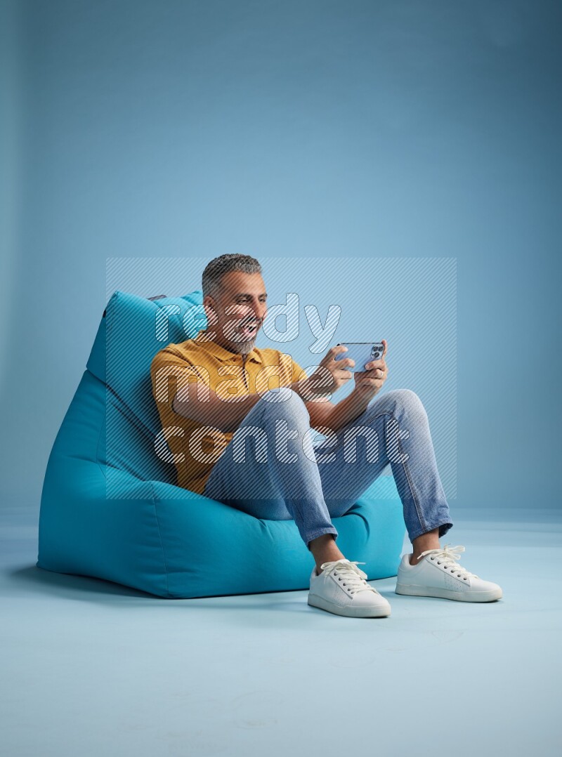 A man sitting on a blue beanbag and playing on phone