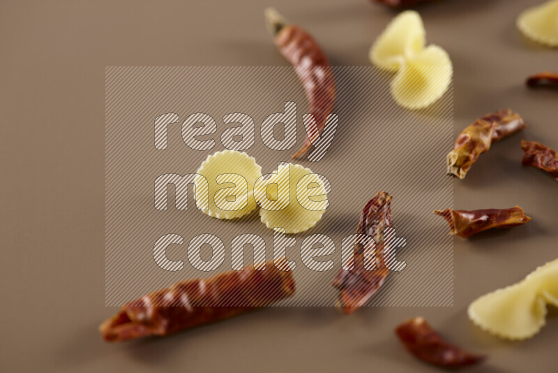 Raw pasta with different ingredients such as cherry tomatoes, garlic, onions, red chilis, black pepper, white pepper, bay laurel leaves, rosemary and cardamom on beige background