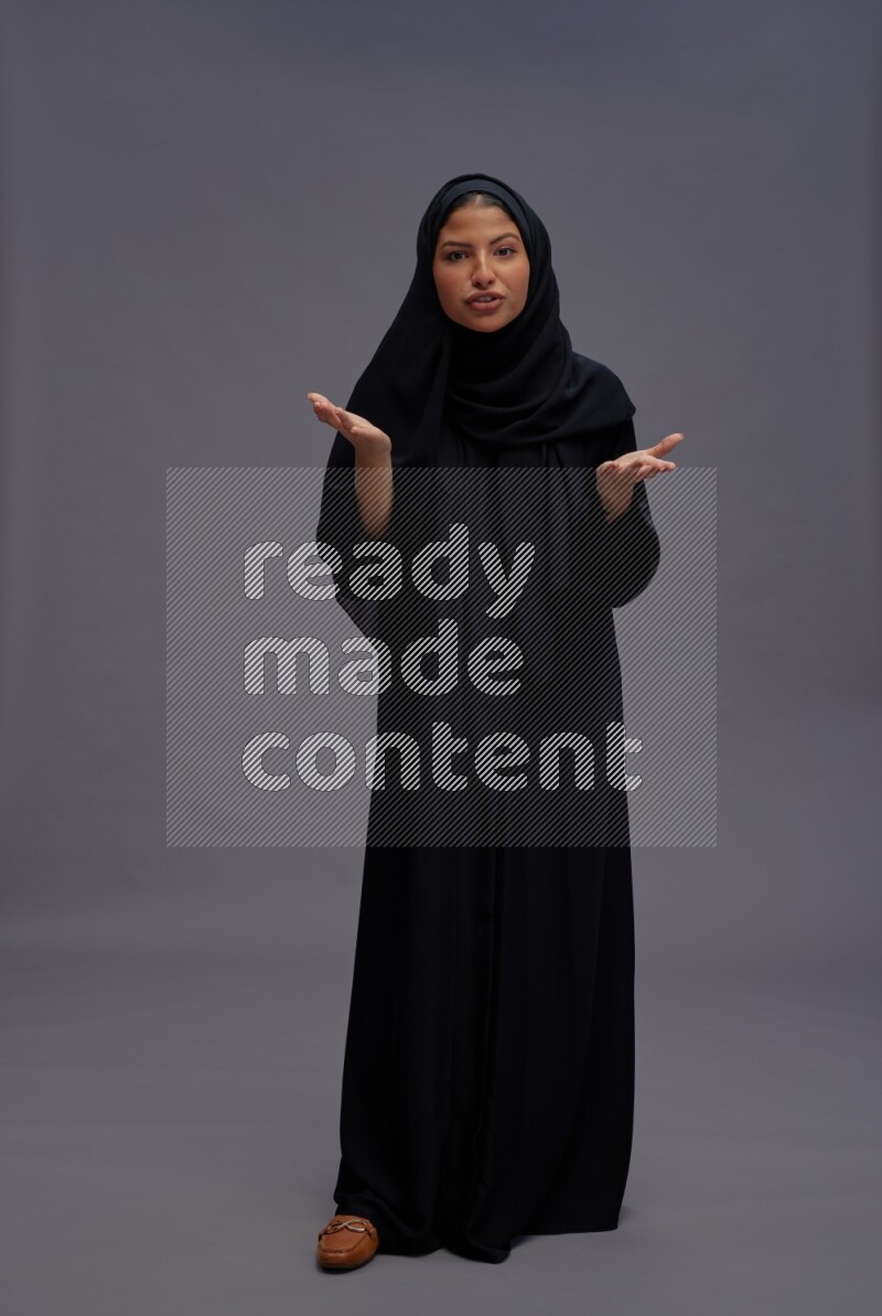 Saudi woman wearing Abaya standing interacting with the camera on gray background