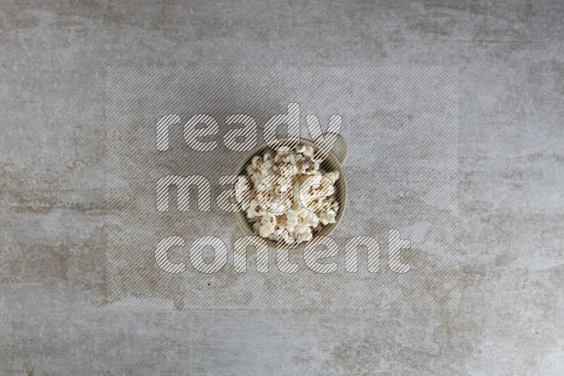 popcorn in a off-white handheld ceramic bowl on a grey textured countertop