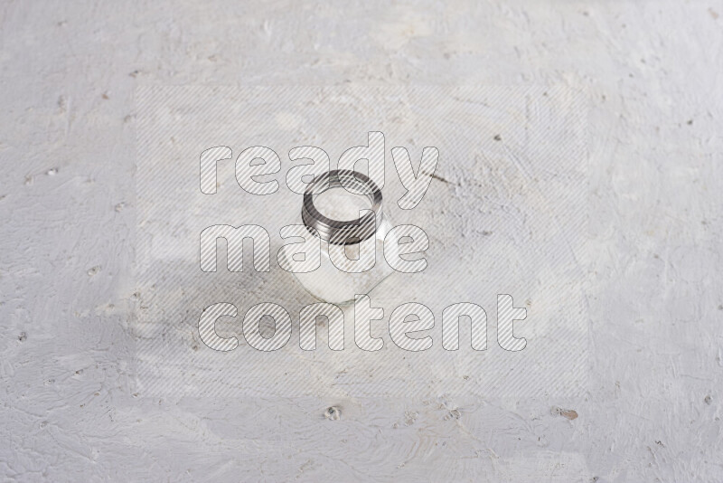 A glass jar full of coarse sea salt crystals on white background