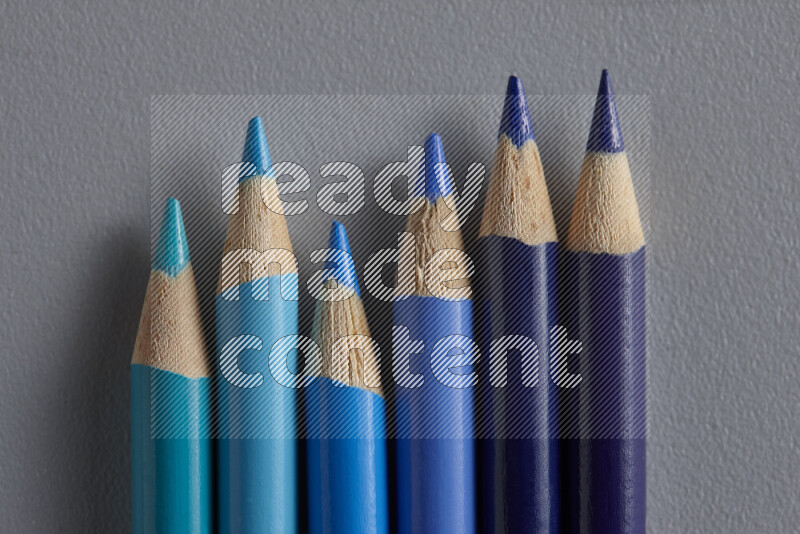 A collection of colored pencils arranged showcasing a gradient of blue hues on grey background