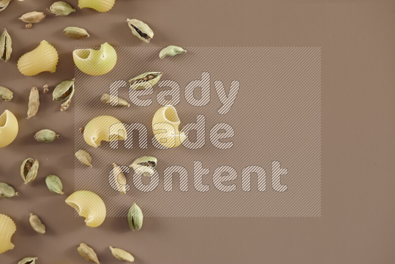 Raw pasta with different ingredients such as cherry tomatoes, garlic, onions, red chilis, black pepper, white pepper, bay laurel leaves, rosemary and cardamom on beige background