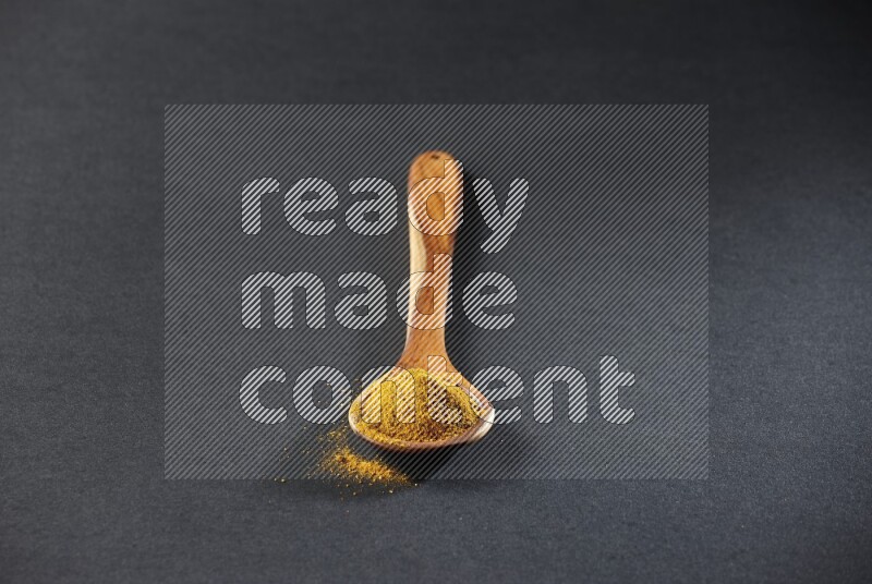 A wooden ladle full of turmeric powder on black flooring