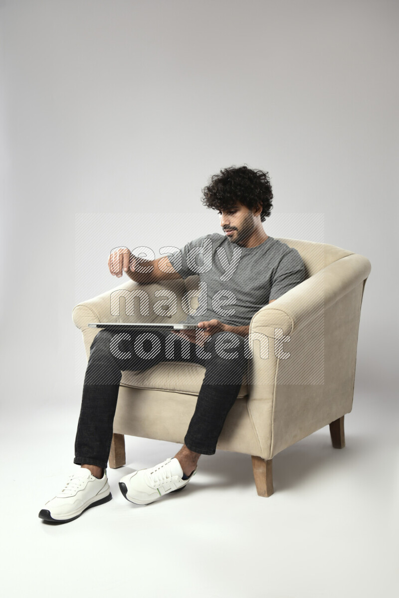 A man wearing casual sitting on a chair holding a laptop on white background
