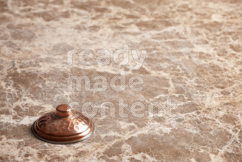 A small copper pot lid on beige marble background