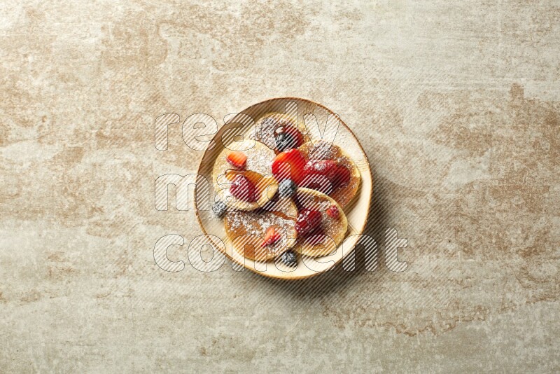 Five stacked mixed berries mini pancakes in an irregular plate on beige background