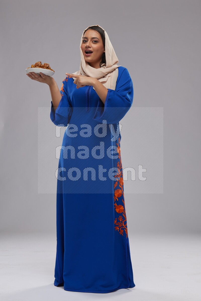 A Saudi woman standing wearing Jalabeya holding a plate of dates