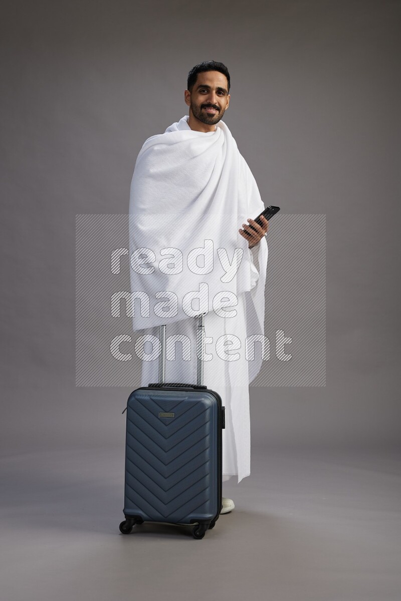 A man wearing Ehram Standing holding traveling bag on gray background