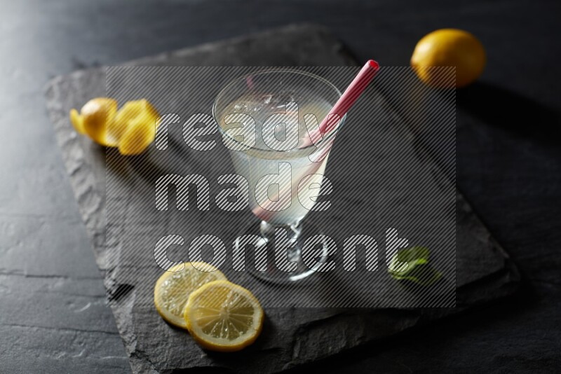 A glass of lemon juice with a straw on black background