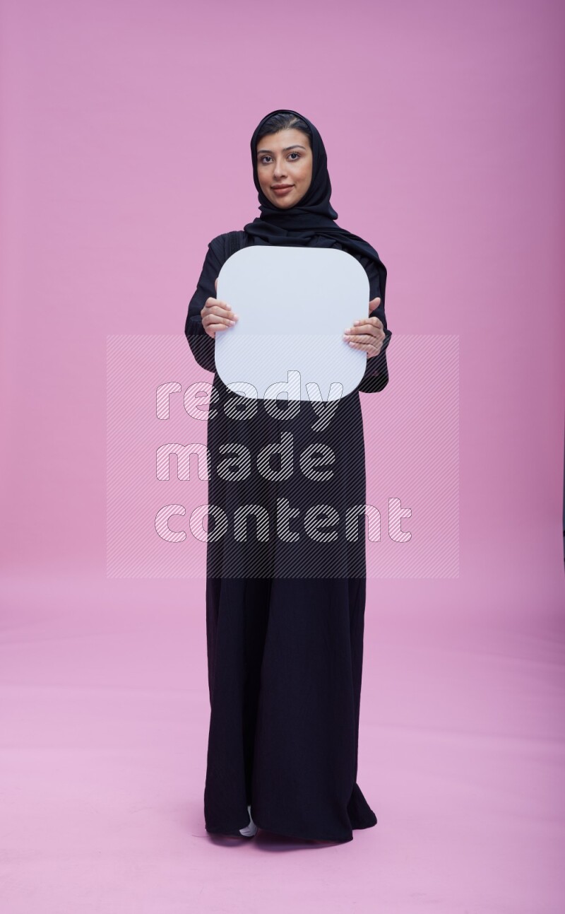 Saudi woman wearing pink ribbon on Abaya standing holding social media signs on pink background