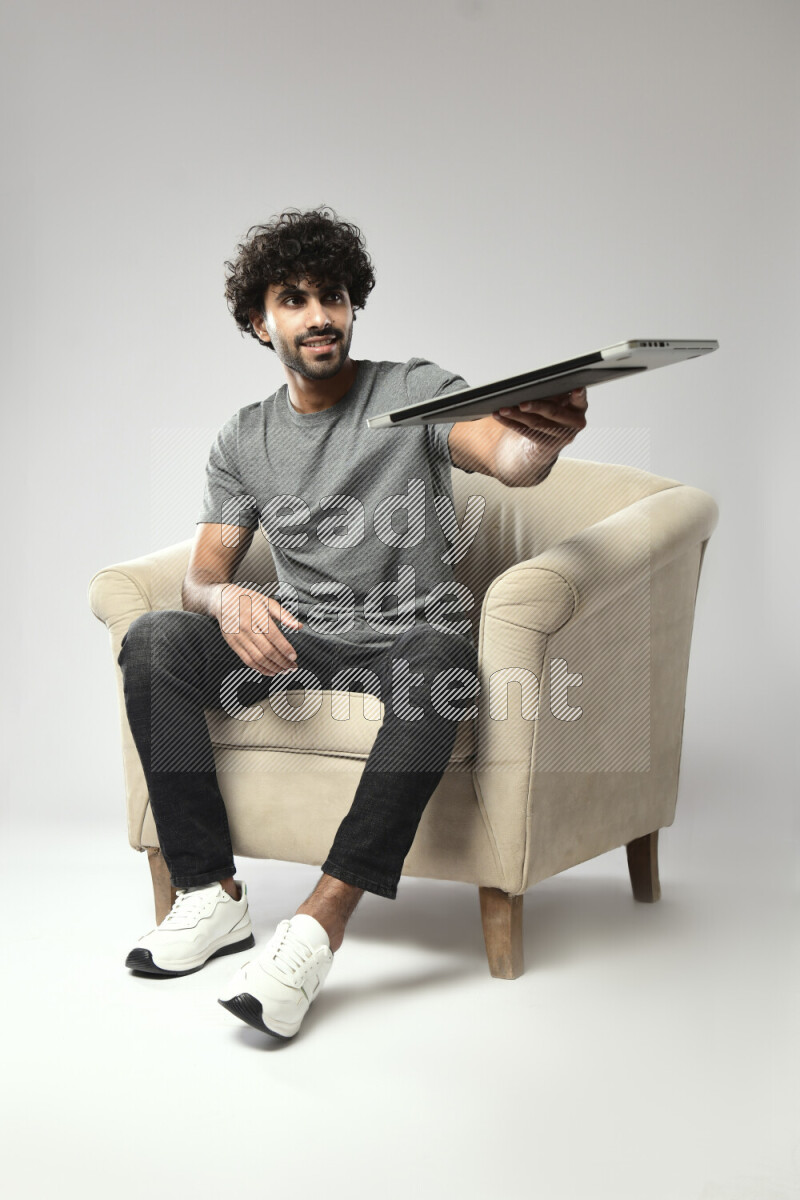 A man wearing casual sitting on a chair holding a laptop on white background