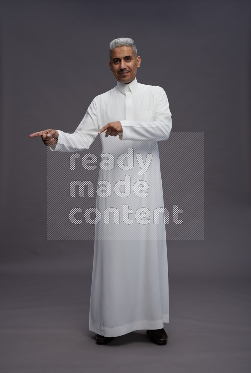 Saudi man wearing thob standing interacting with the camera on gray background