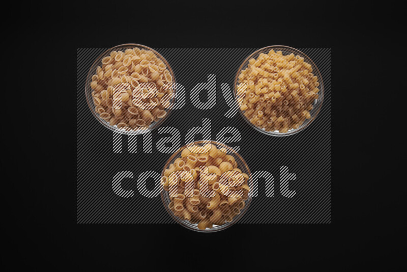 Different pasta types in glass bowls on black background