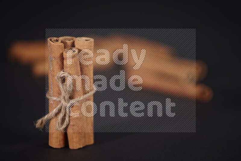 4 Cinnamon sticks stacked and bounded with more sticks in the background on black flooring