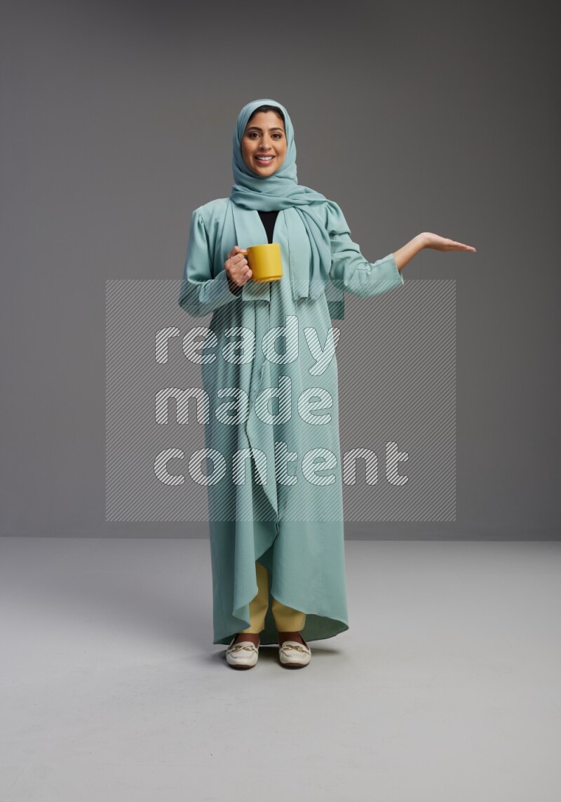 Saudi Woman wearing Abaya standing  holding a mug on Gray background