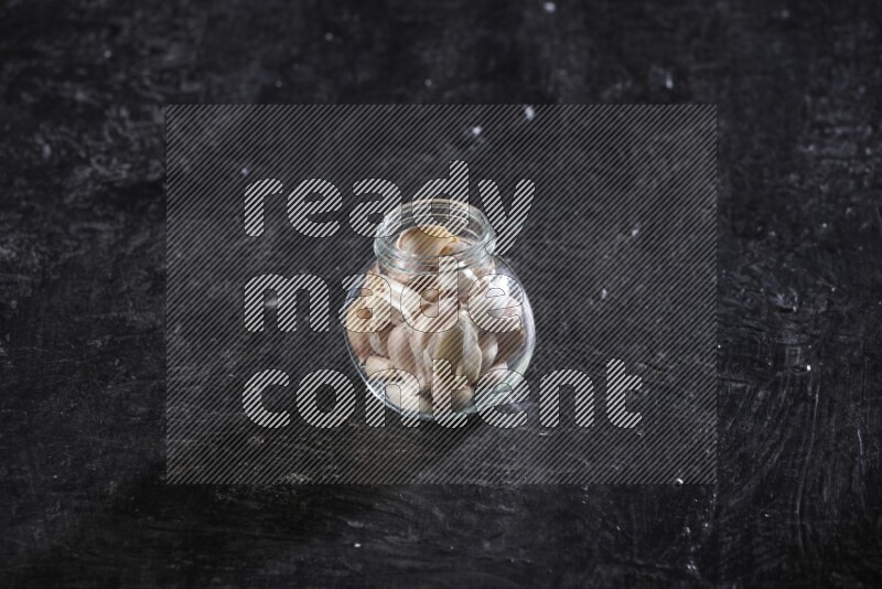 A glass spice jar full of garlic cloves on a textured black flooring