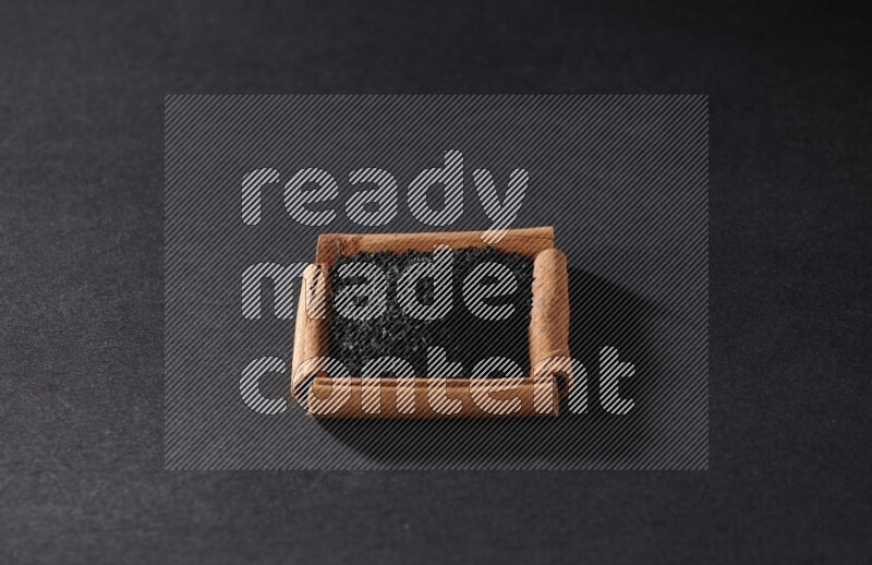 أربعة من أعواد القرفة مكونة شكل مربع بداخلها حبة البركة علي خلفية سوداء