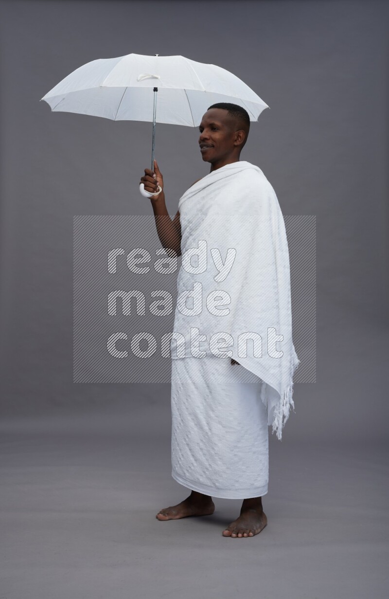 A man wearing Ehram Standing holding umbrella on gray background