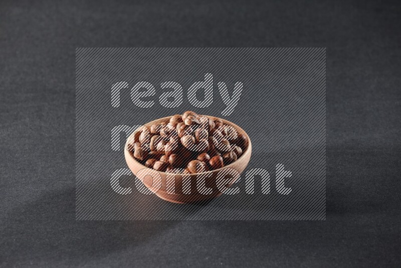 A wooden bowl full of peeled hazelnuts on a black background in different angles